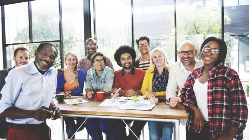 A diverse group of employees stand around a table and discuss managing generations in the workplace