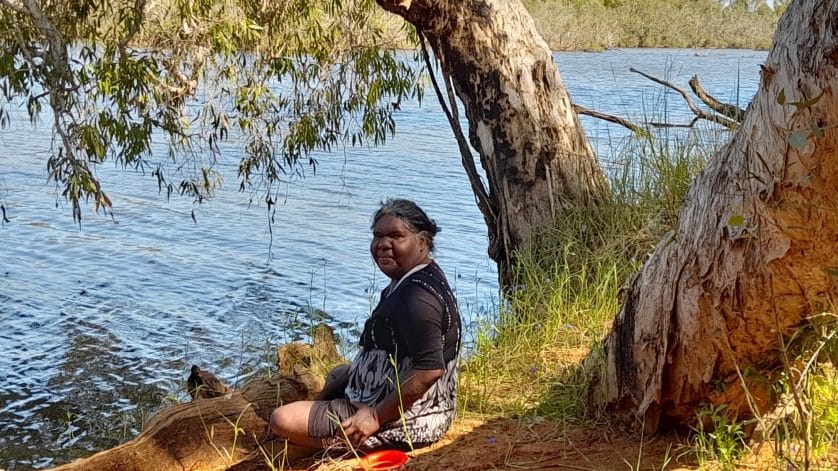 Gaylene, an Indigenous woman sits near the bank of the Nicholson river under a paperbark tree