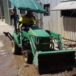 Employee intern Rex Liddy sccops up mud left by flooding with a green tractor